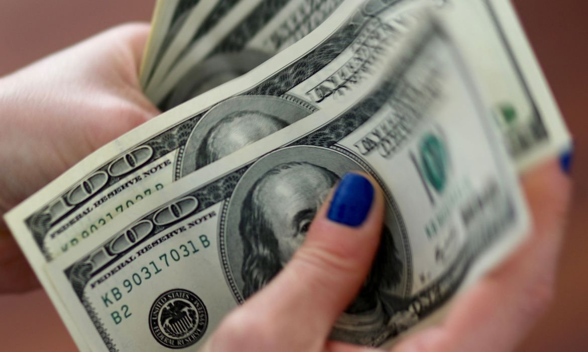 dolar #Pracegover Foto: Na imagem uma mulher segura algumas notas em dólar