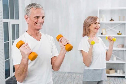 idosos #Pracegover Foto: Na imagem um homem e uma mulher, ambos idosos, realizam exercícios físicos em um cômodo amplo em casa