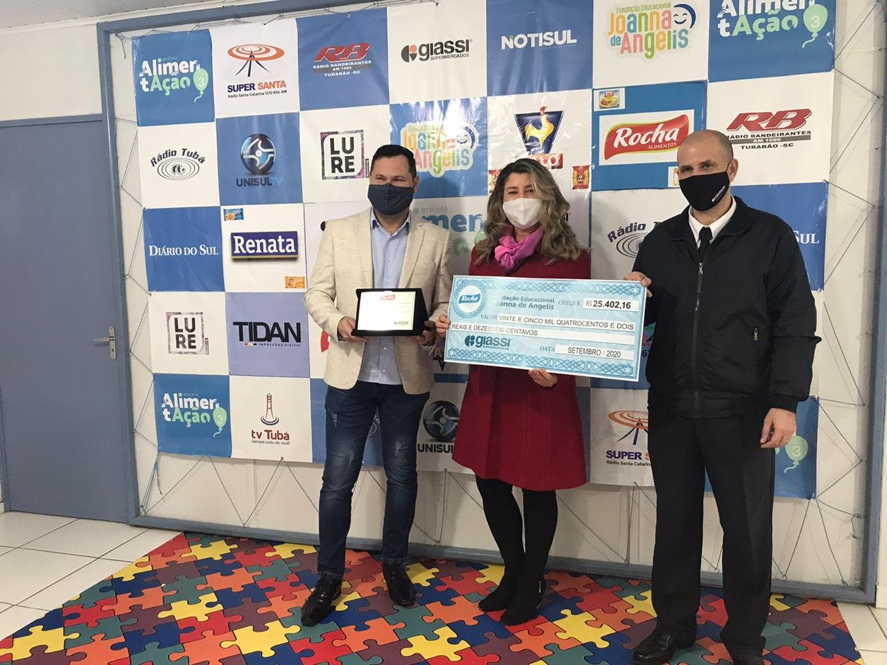Joanna de Angelis #Pracegover Foto: Na imagem há três pessoas, uma delas a presidente da Fundação Educacional Joanna de Angelis, Sandra Nazário que segura o cheque simbólico de mais de R$ 25 mil