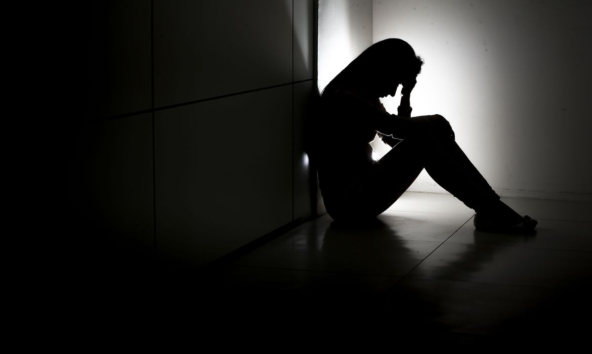 mulher #Pracegover Foto: Na imagem há uma mulher sentada, triste e com pensamento suicida