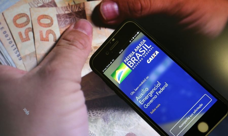 auxilio_emergencial_caixa_15 #Pracegover Foto: na imagem há cédulas de R$ 50 e 100. Uma pessoa segurando um celular