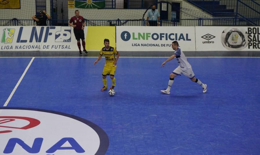 futsal #Pracegover Foto: na imagem há dois jogadores de times opostos, um árbitro e uma bola