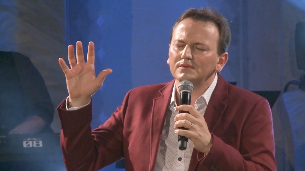 padre #Pracegover Foto: na imagem há um homem de terno, com uma mão levantada e a outra segurando um microfone