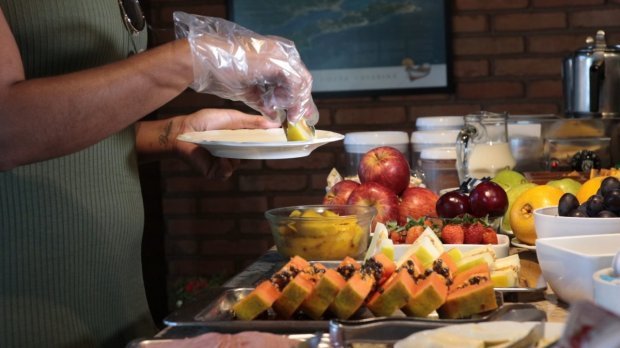 hoteis_pousadas #Pracegover Foto: na imagem há muitas frutas, uma pessoa com luvas e um prato