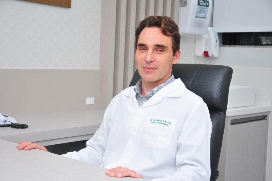 médico #Prcegover Foto: na imagem há um homem de jaleco, uma mesa e uma cadeira