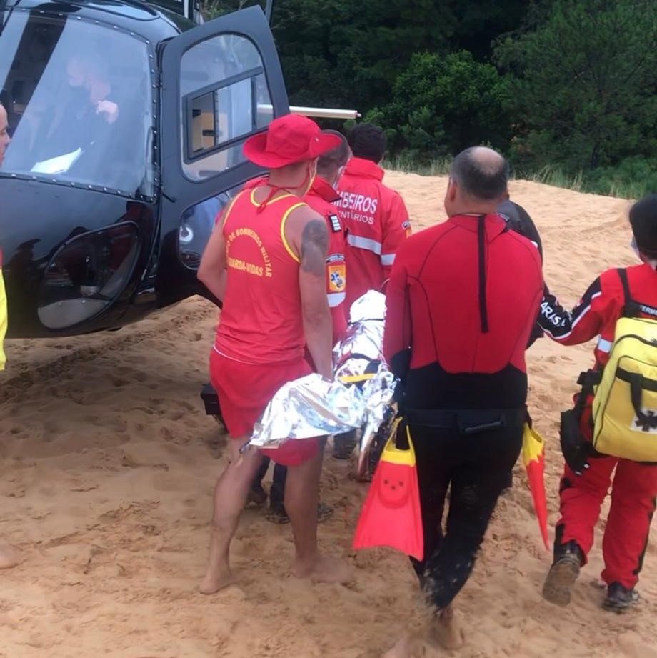 Adolescente de 16 anos sofre trauma na coluna após mergulhar em parte rasa de lagoa em Jaguaruna #Pracegover Na foto, Bombeiros resgatam o adolescente e o levam para o helicóptero