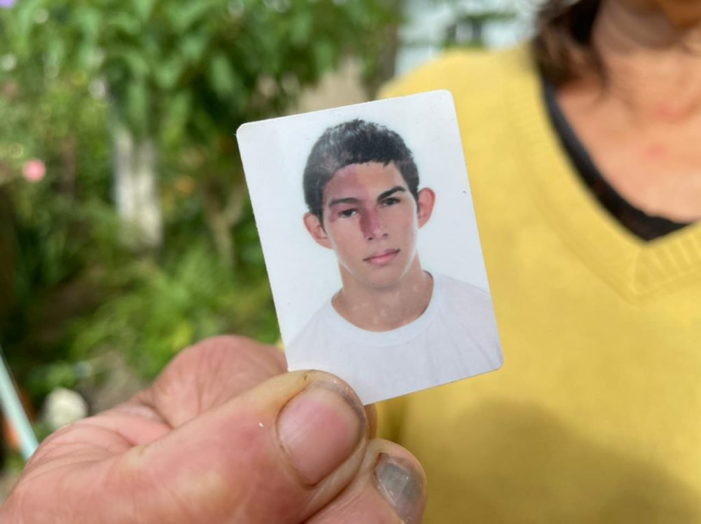 Adriano #Pracegover Foto: na imagem há uma mulher segurando um retrato 3/4 de um jovem