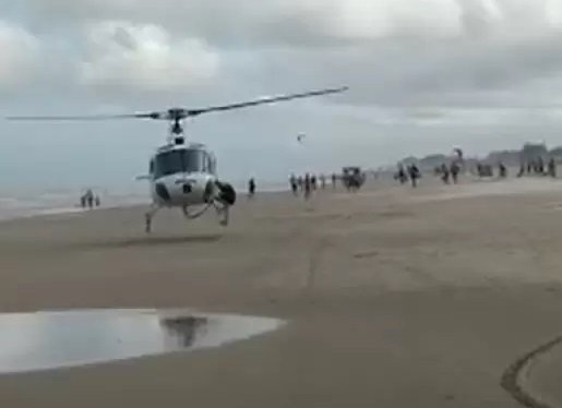 heli #Pracegover Foto: na imagem há um helecoptero, diversas pessoas, areia e água
