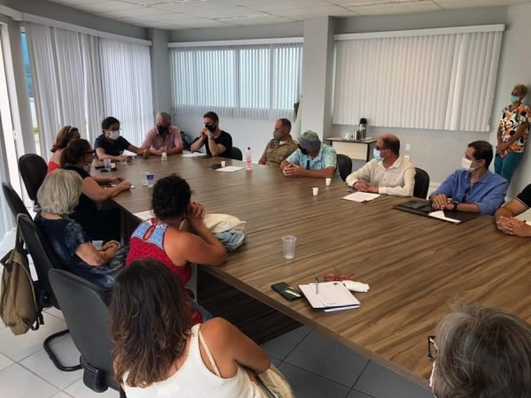 reunião #Pracegover Foto: na imagem há diversas pessoas, uma mesa e papeis