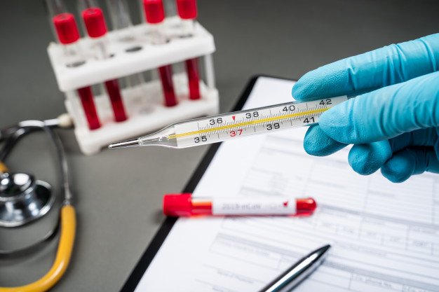 Tubarão registra mais 1 morte por Covid-19, ao todo são 192 óbitos #Pracegover Na foto, um profissional segura um termômetro, ao fundo da imagem há um caderno de anotações, canetas e vários tubos com sangue para exame