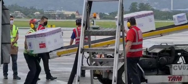 vacinas coronavac #Pracegover Foto: na imagem há homens, uma caixa e pista