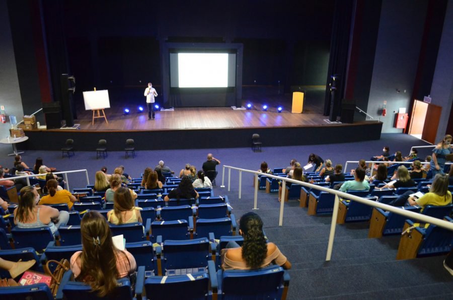 capacitação #Pracegover Foto: na imagem há arquibancadas, pessoas, um palco com telão