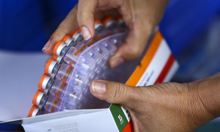 #Pracegover Foto: na imagem há duas mãos e muitas doses de vacinas