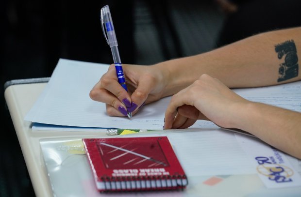 ensino superior #Pracegover Foto: na imagem há dois braços, duas mãos, uma caneta, um bloco de notas e um caderno