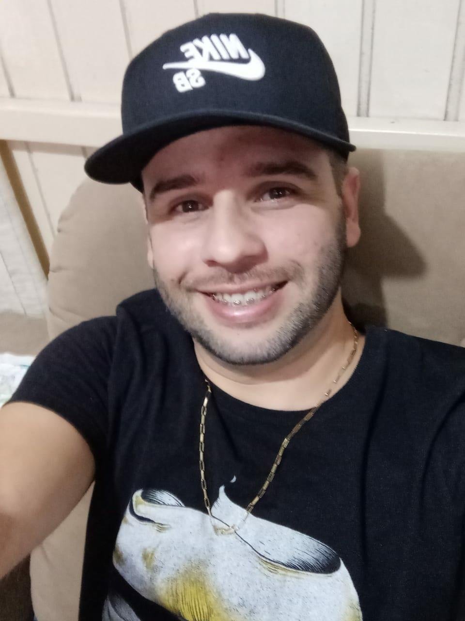 moises #Pracegover Foto: na imagem há um homem de camiseta preta, boné preto e corrente