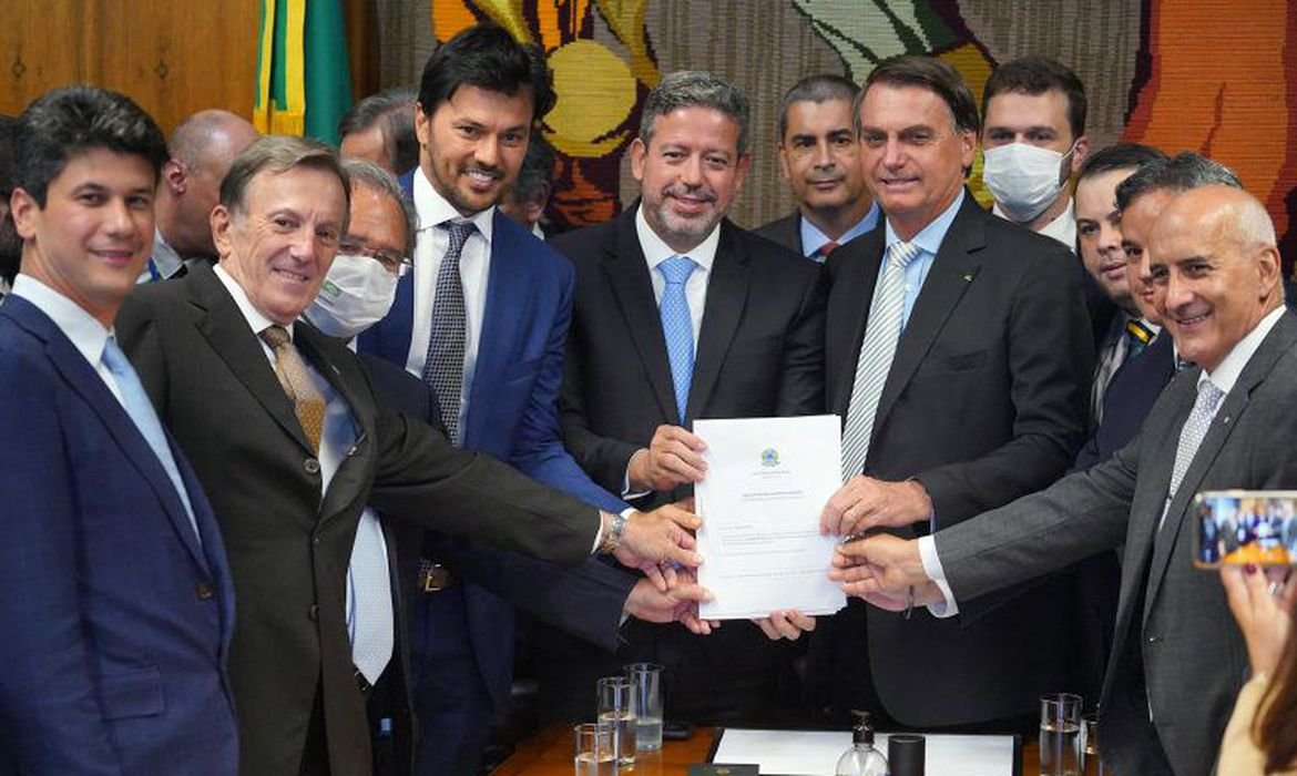 pl #Pracegover Foto: na imagem há diversos homens de terno segurando folhas