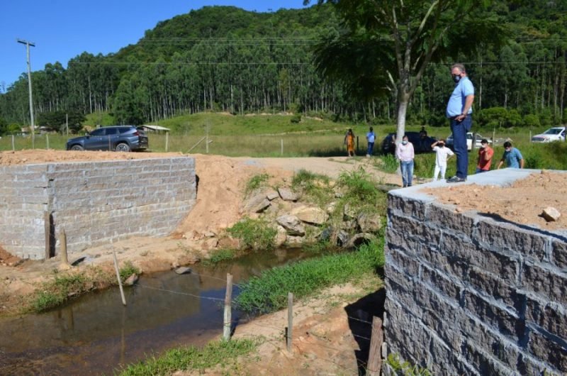 ponte #Pracegover Foto: na imagem há um rio, árvores, pessoas e um carro