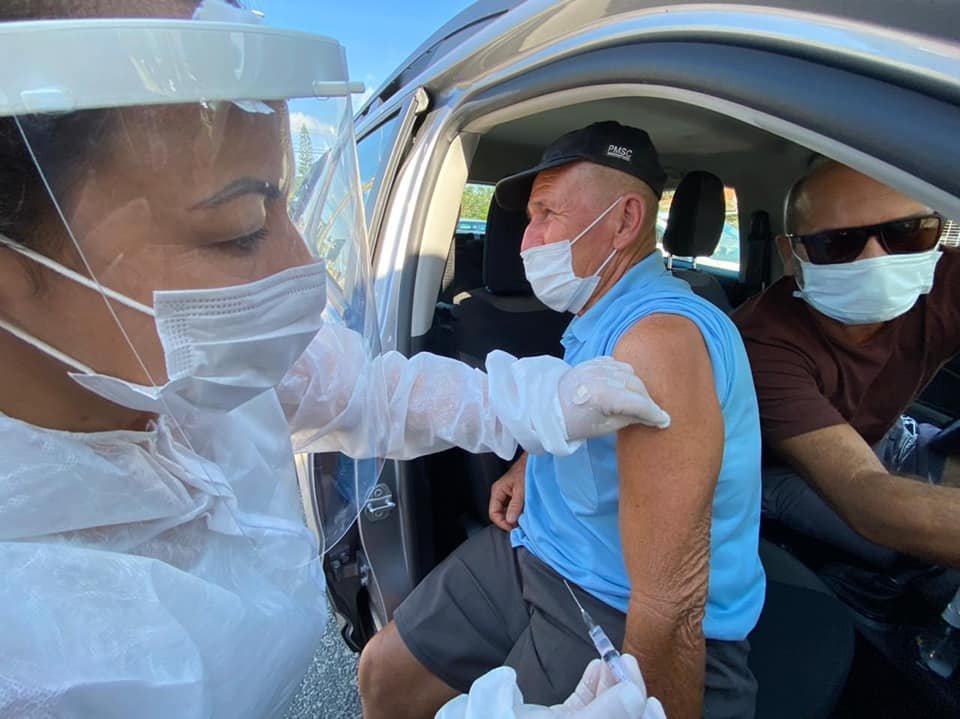 drive #Pracegover Foto: na imagem há três pessoas, uma delas é vacinada