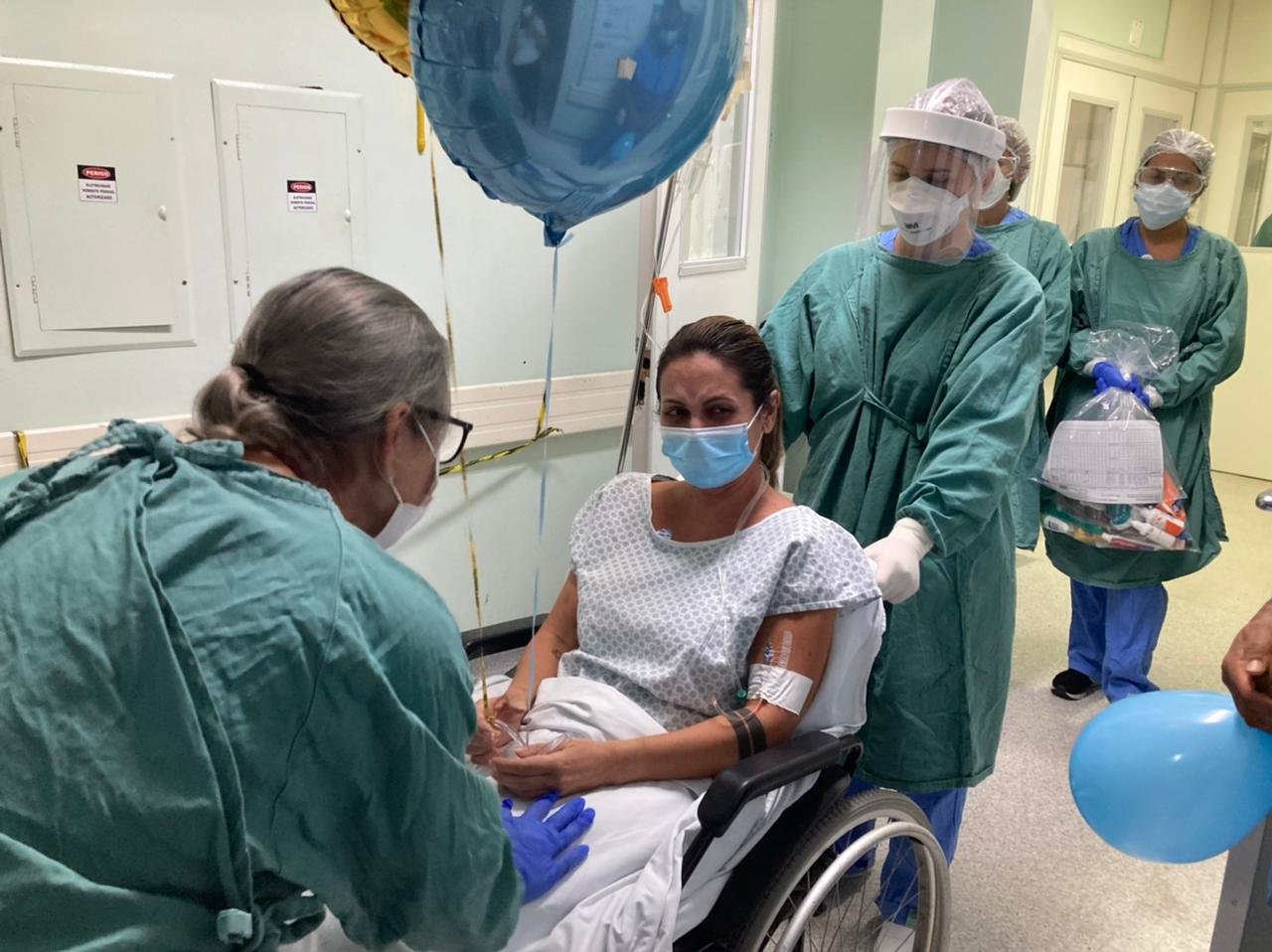 paciente covid #Pracegover Foto: na imagem há uma mulher na cadeira de rodas e outras pessoas próximas a ela, Há balões no local