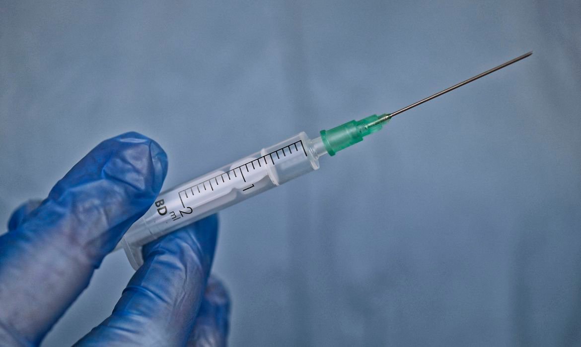 vacina 2 #Pracegover Foto: na imagem há uma seringa, agulha e uma mão com luva azul