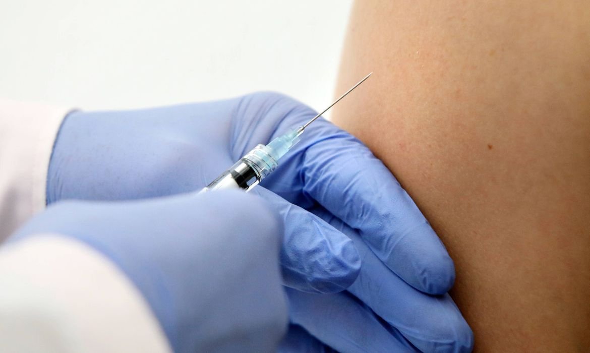 vacina #Pracegover Foto: na imagem há um braço, mãos e uma seringa com agulha