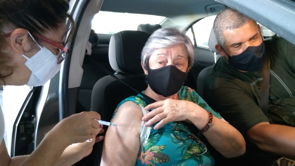 vacinação #Pracegover Foto: na imagem há três pessoas, uma delas aplicando e a outra recebendo a vacina.