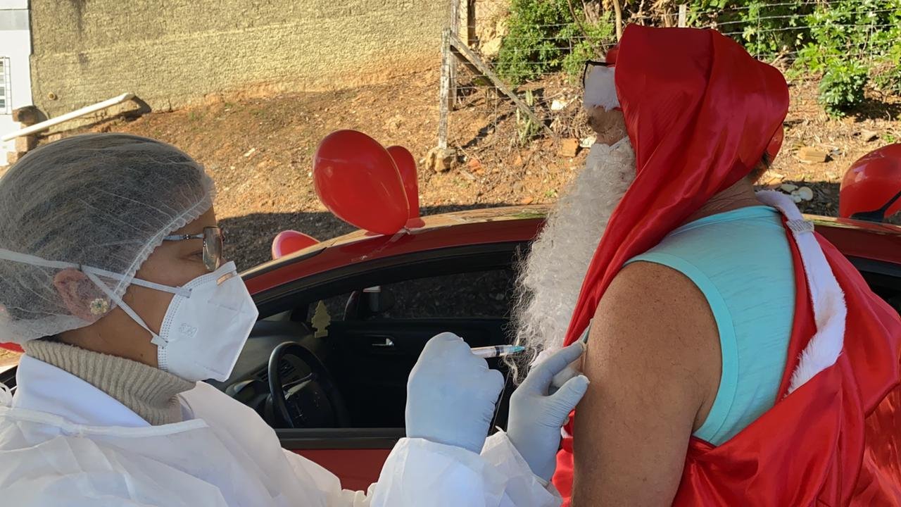 Papai Noel’ é vacinado em Cocal do Sul contra a Covid-19 #Pracegover Na foto, profissional da saúde aplicando vacina em um homem vestido de Papai de Noel