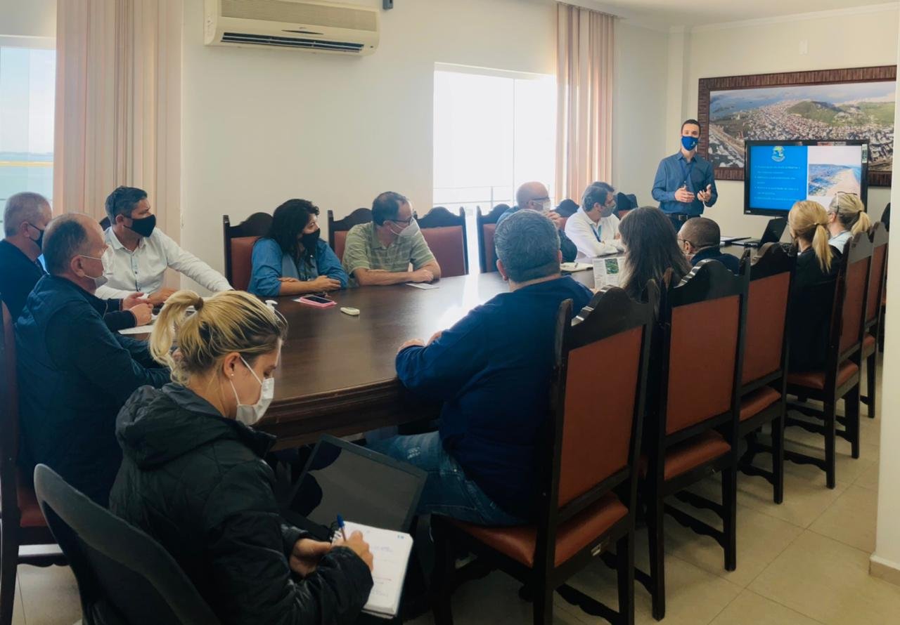 trato #Pracegover Foto: na imagem há várias pessoas, uma mesa e cadeiras