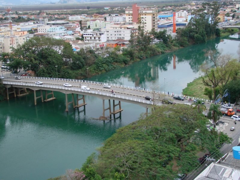 Tubarão rio #Pracegover Foto: na imagem há um rio, uma ponte, árvores, construções e carros