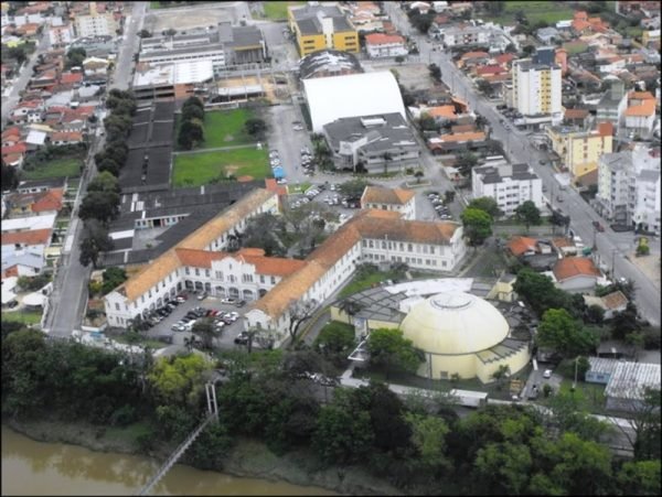 unisul-suspende-atividades-academicas-no-campus-tubarao-1 #Pracegover Foto: na imagem há construções, árvores e rio