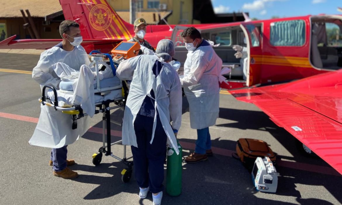 covid ms #Pracegover Foto: na imagem há profissionais de saúde, uma maca com aparelhos e uma aeronave