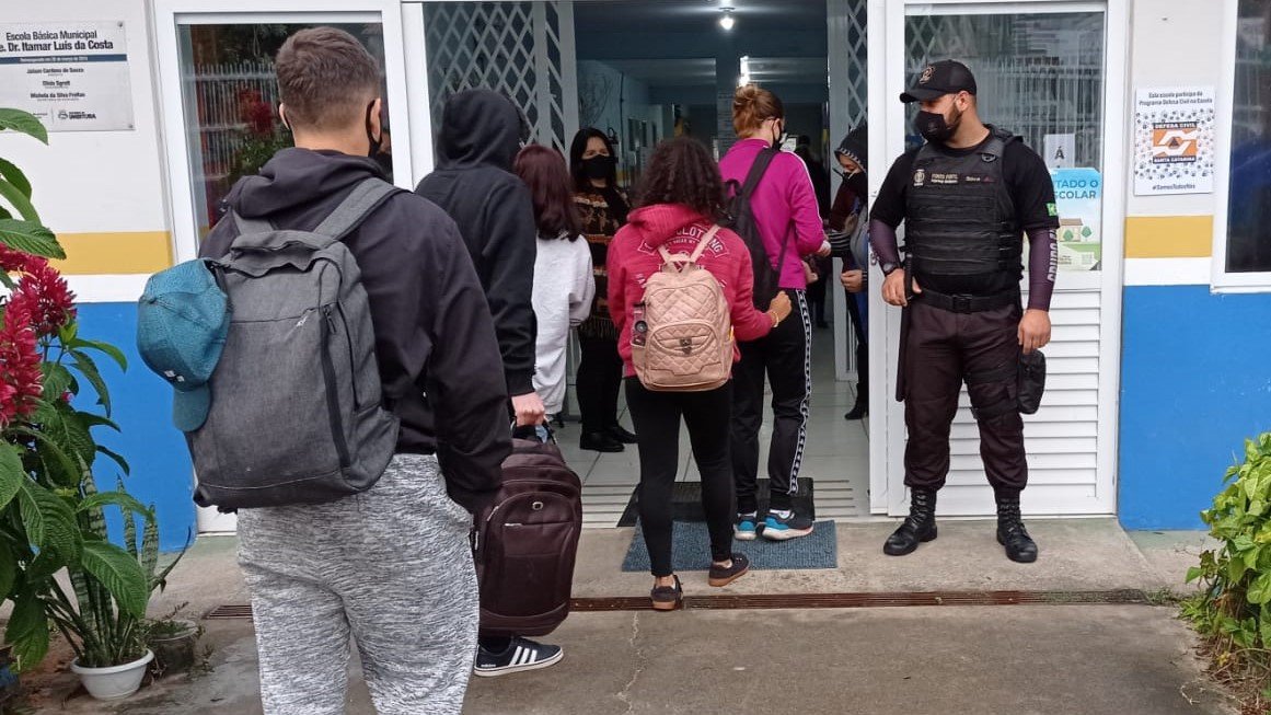 Mensagem sobre invasão criminosa em escola de Imbituba é falsa, afirma a prefeitura #Pracegover Na foto, alunos entrando em uma escola e um agente de segurança na porta