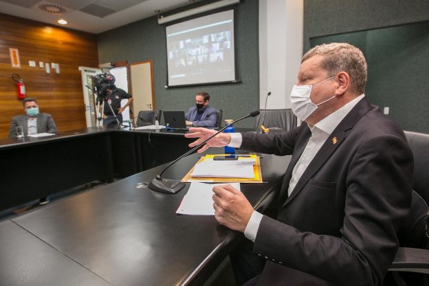 reunião #Pracegover Foto: na imagem há pessoas, uma mesa, folhas, canetas e microfones