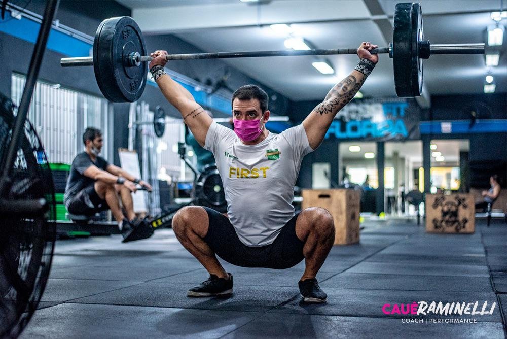 Cauê #Pracegover foto: na imagem há um homem de bermuda preta, camiseta clara e de máscara. Ele está levantando peso (treinando)