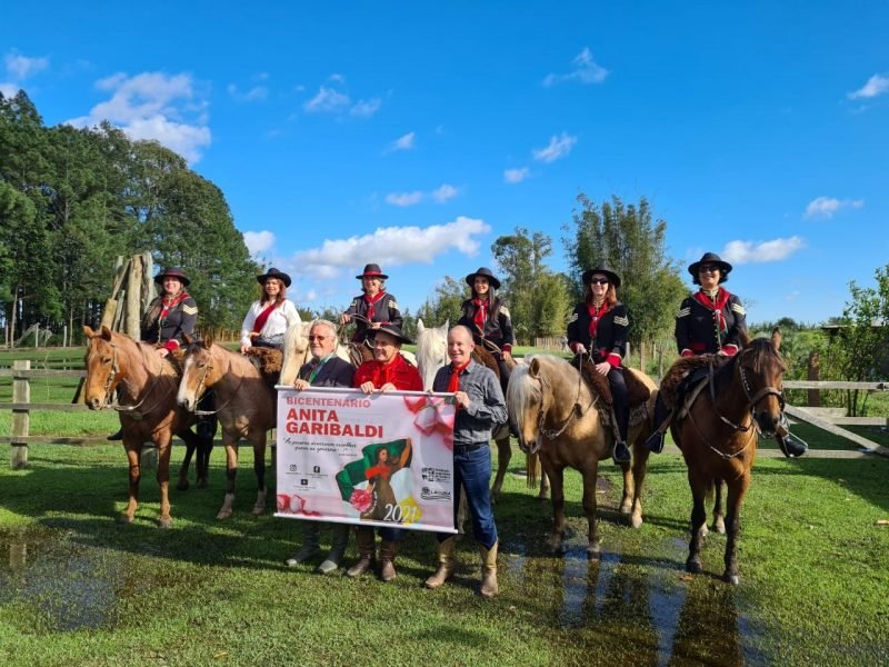 Bicentenário #Pracegover foto: na imagem há pessoas, equinos, árvores e um cartaz
