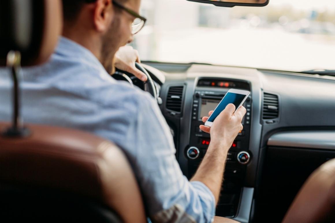 dirigir-segurando-telefone-celular #Pracegover foto: na imagem há um homem dirigindo e segurando o celular