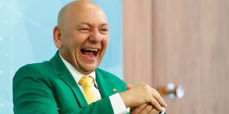 hang luciano #Pracegover foto: na imagem há um homem de terno verde, camisa branca e gravata amarela