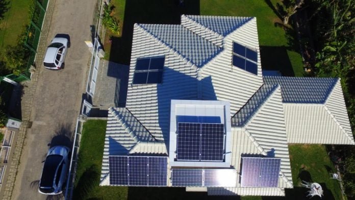 Energia-Foltovoltaica_Divulgação-Alesc #Pracegover foto: na imagem há o telhado de uma casa, placas solares, veículos, via e árvores