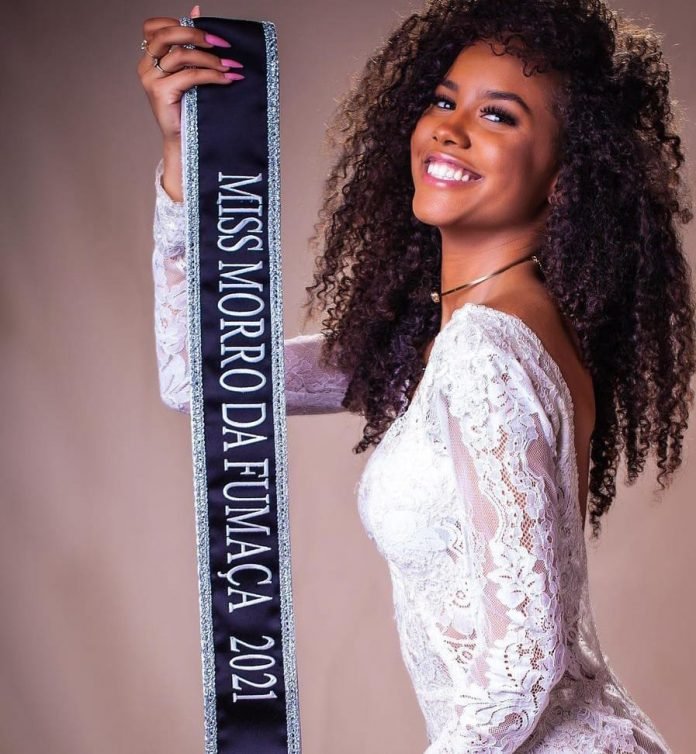 miss #Pracegover foto: na imagem há uma mulher segurando uma faixa