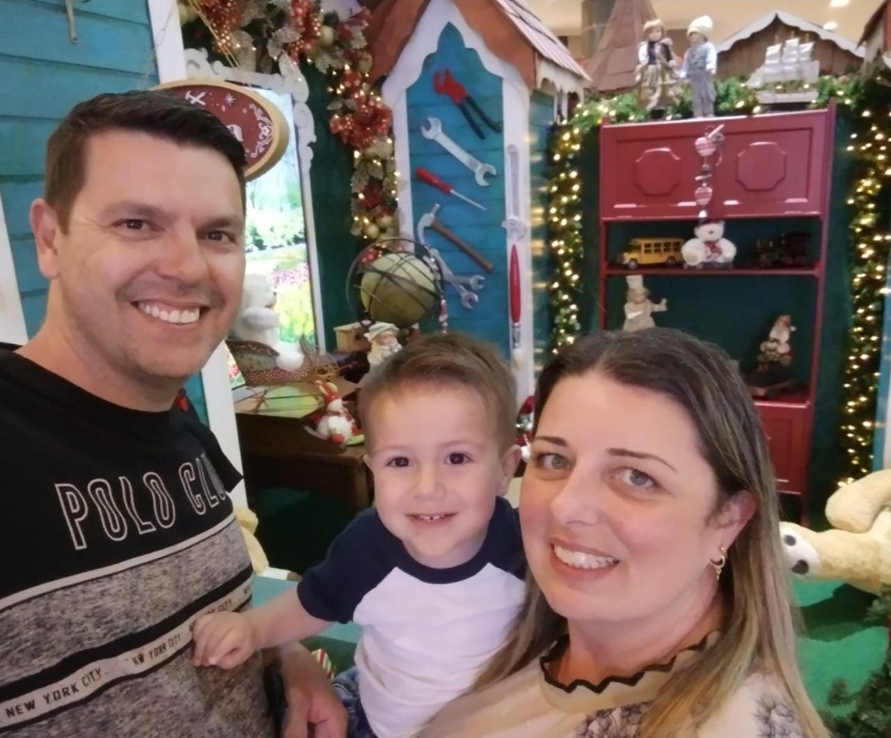 trio #Pracegover foto: na imagem há um homem, uma mulher e um menino. Há também muitos brinquedos