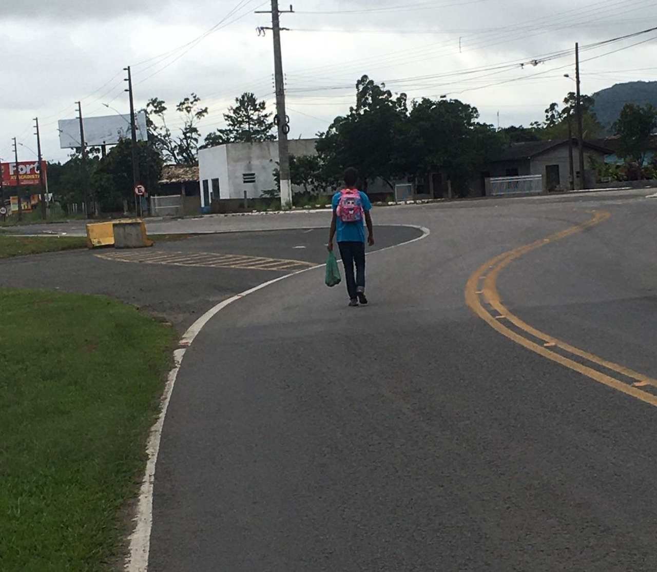luciano-desaparecido #Pracegover Foto: na imagem há um homem com mochila nas costas e uma sacola nas mãos, uma via, casas, gramado , árvores e postes