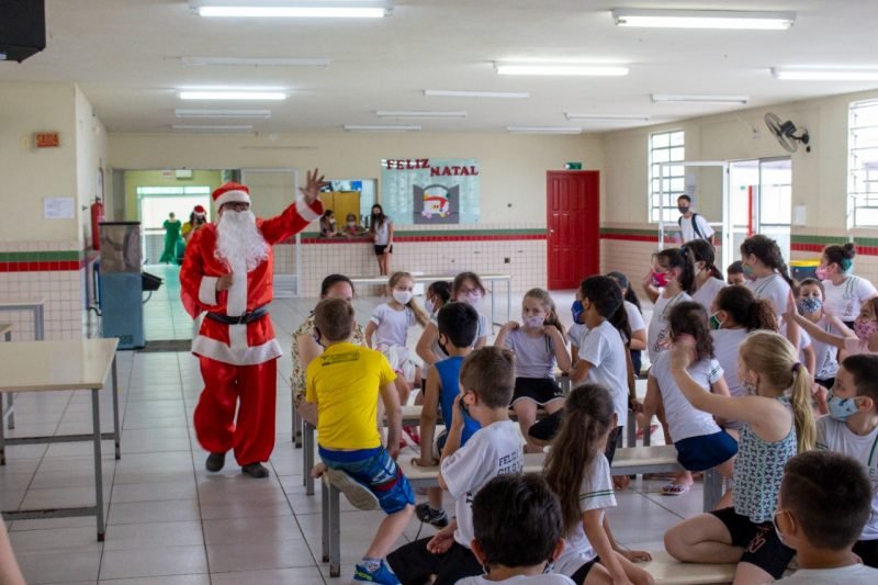 papai noel e crianças #Pracegover Foto: na imagem há um papai noel, crianças e bancos