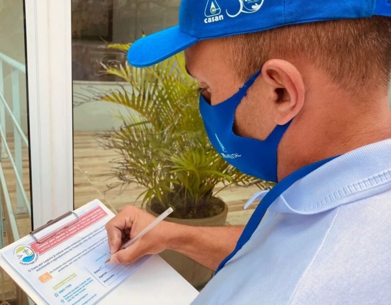 trato #Pracegover foto: na imagem há um homem de boné e máscara, caneta, folhas e árvore