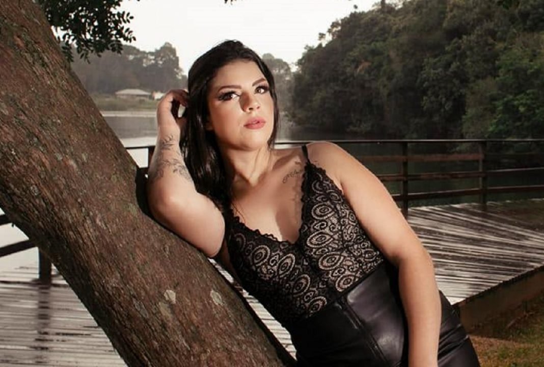 amanda_albach #Pracegover Foto: na imagem há uma jovem de roupa preta, um lago, uma estrutura de madeira e árvores
