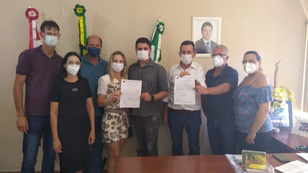São Martinho 1 #Pracegover Foto: na imagem há várias pessoas, quatro delas seguram documentos nas mãos, bandeiras, mesa e um quadro