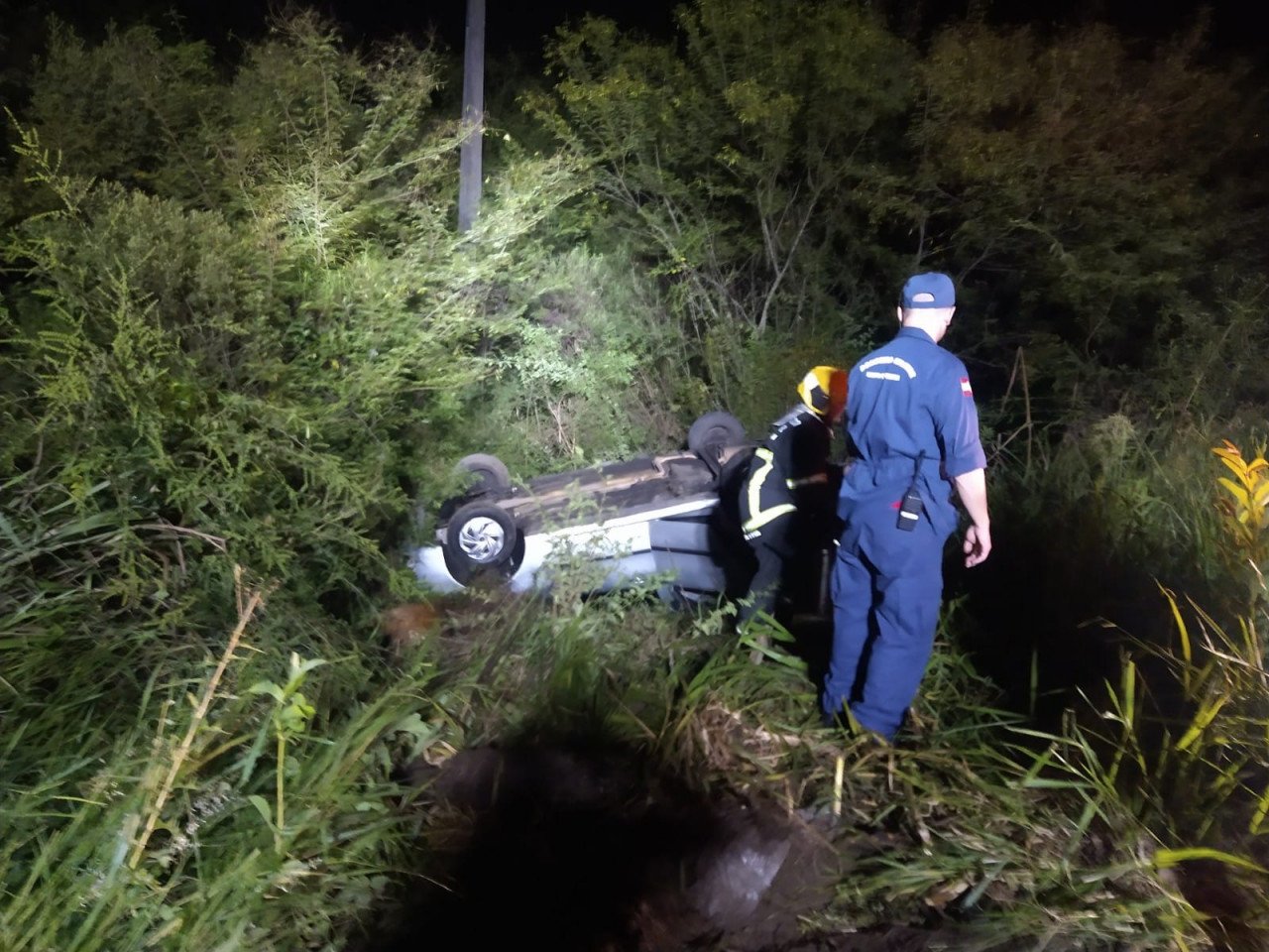 Capotamento em Criciúma #PraCegoVer Na foto, dois bombeiros militares fazem o resgate de um homem em um carro capotado no meio do mato