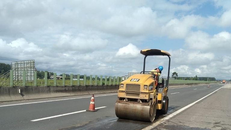 #PraCegoVer Na foto, um rolo compressor sobre uma estrada