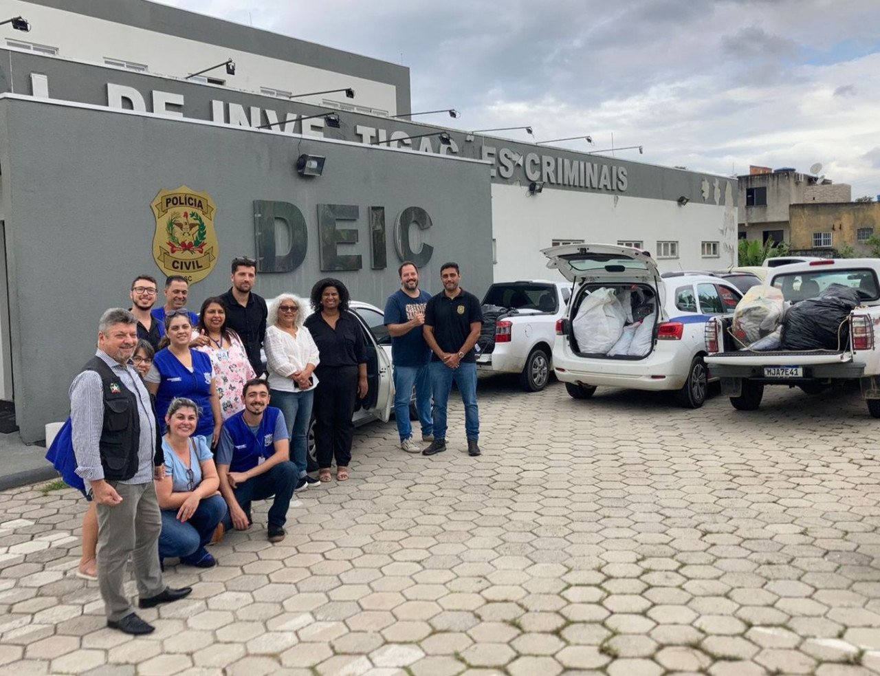 Etiqueta Segura #PraCegoVer Na foto, um grupo de pessoas e dois carros cheios de roupas