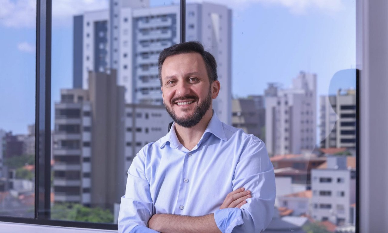 Pepê Collaço #PraCegoVer Na foto, um homem na frente de uma janela, com prédios atrás