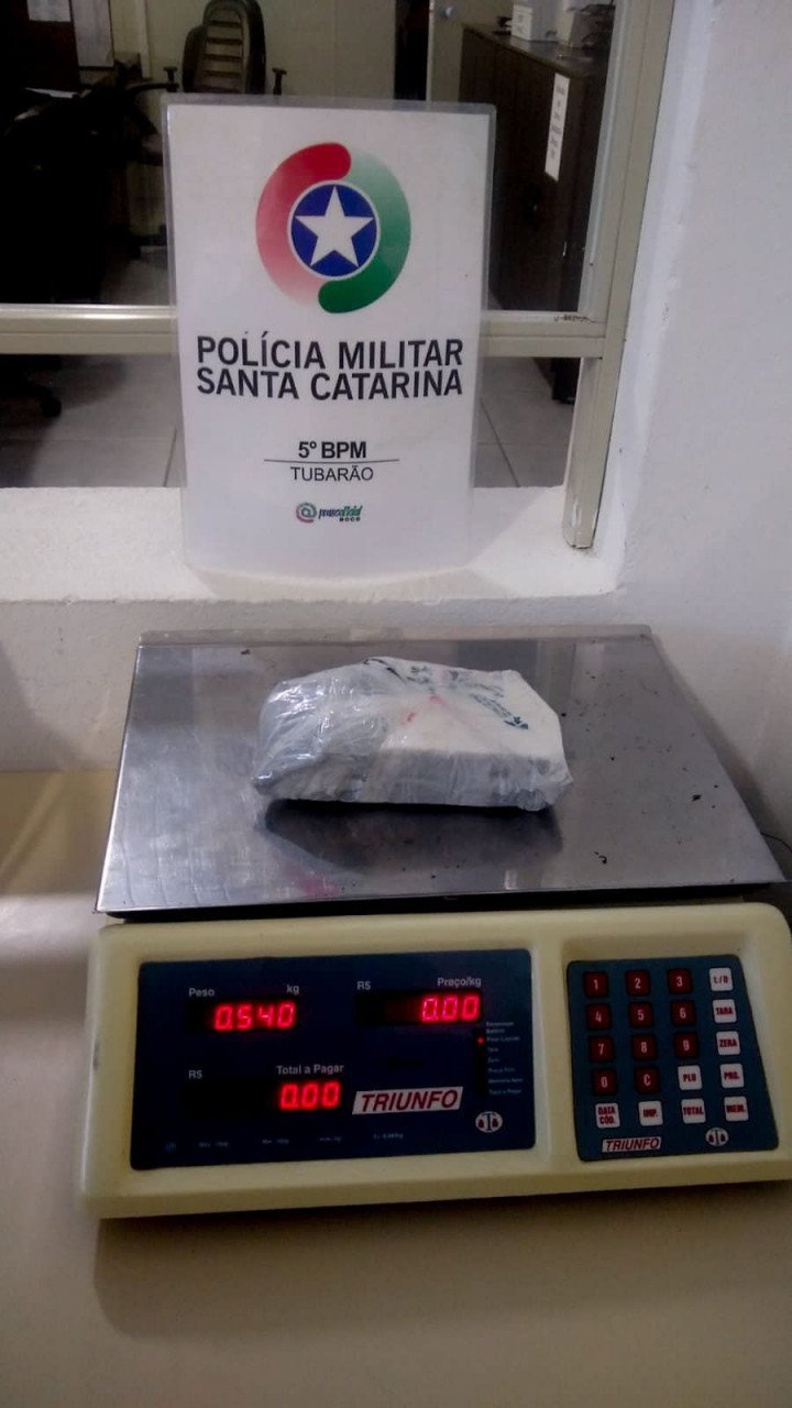 Droga Tubarão #PraCegoVer Na foto, o símbolo da Polícia Militar de Santa Catarina e um pacote com drogas em cima de uma balança